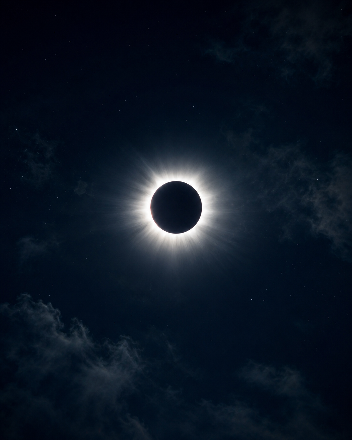Fotografía de un eclipse solar total: el disco negro rodeado de una corona luminosa sobre un cielo nocturno con nubes